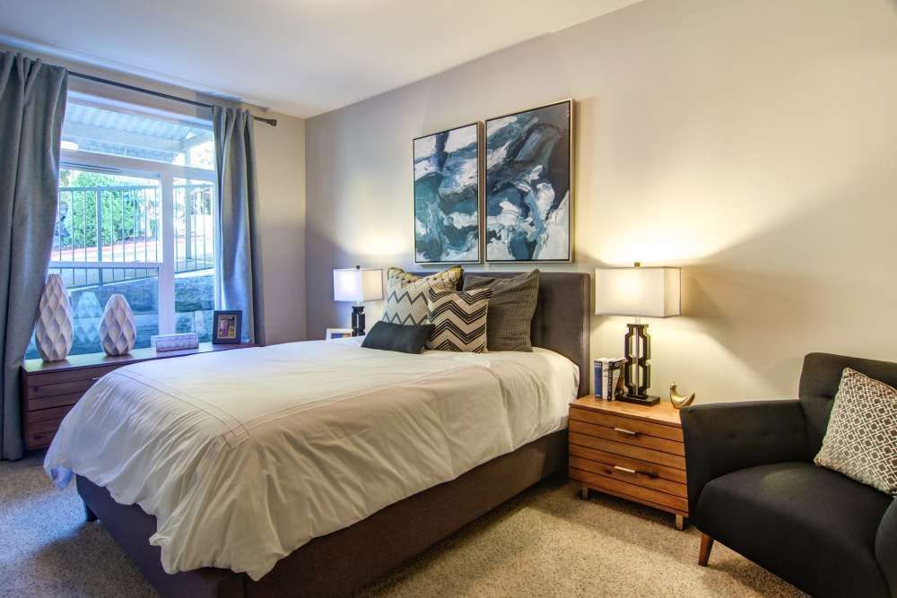 Bedroom with a bed, nightstands, chair, window, artwork, and beige carpet.