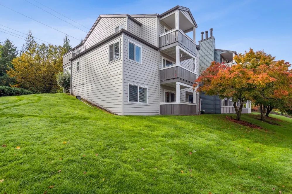 Multi-story residential building with balconies on a grassy hillside, trees with autumn foliage.