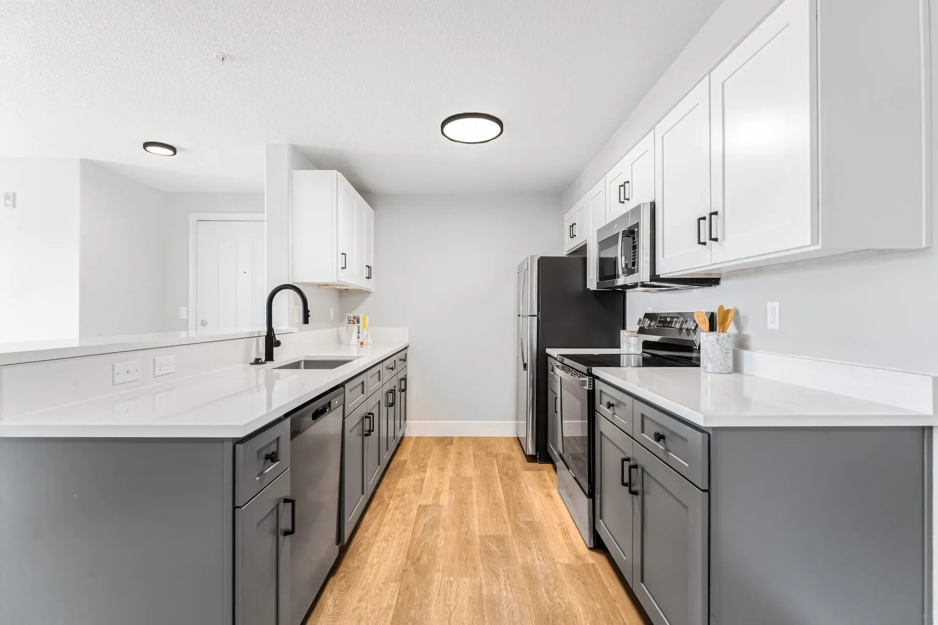 Modern kitchen with gray and white cabinets, stainless steel appliances, and wood-look flooring.