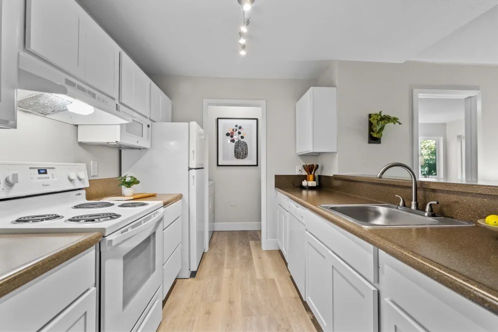 White kitchen with appliances and cabinets, wood-look countertops, and light wood flooring.