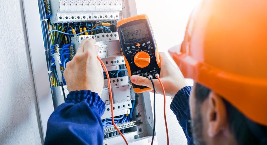 Technician using a multimeter to test wiring inside an electrical control panel