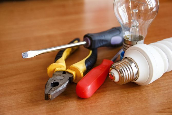 Pliers, screwdriver, light bulb, and red-handled tool on a wooden table
