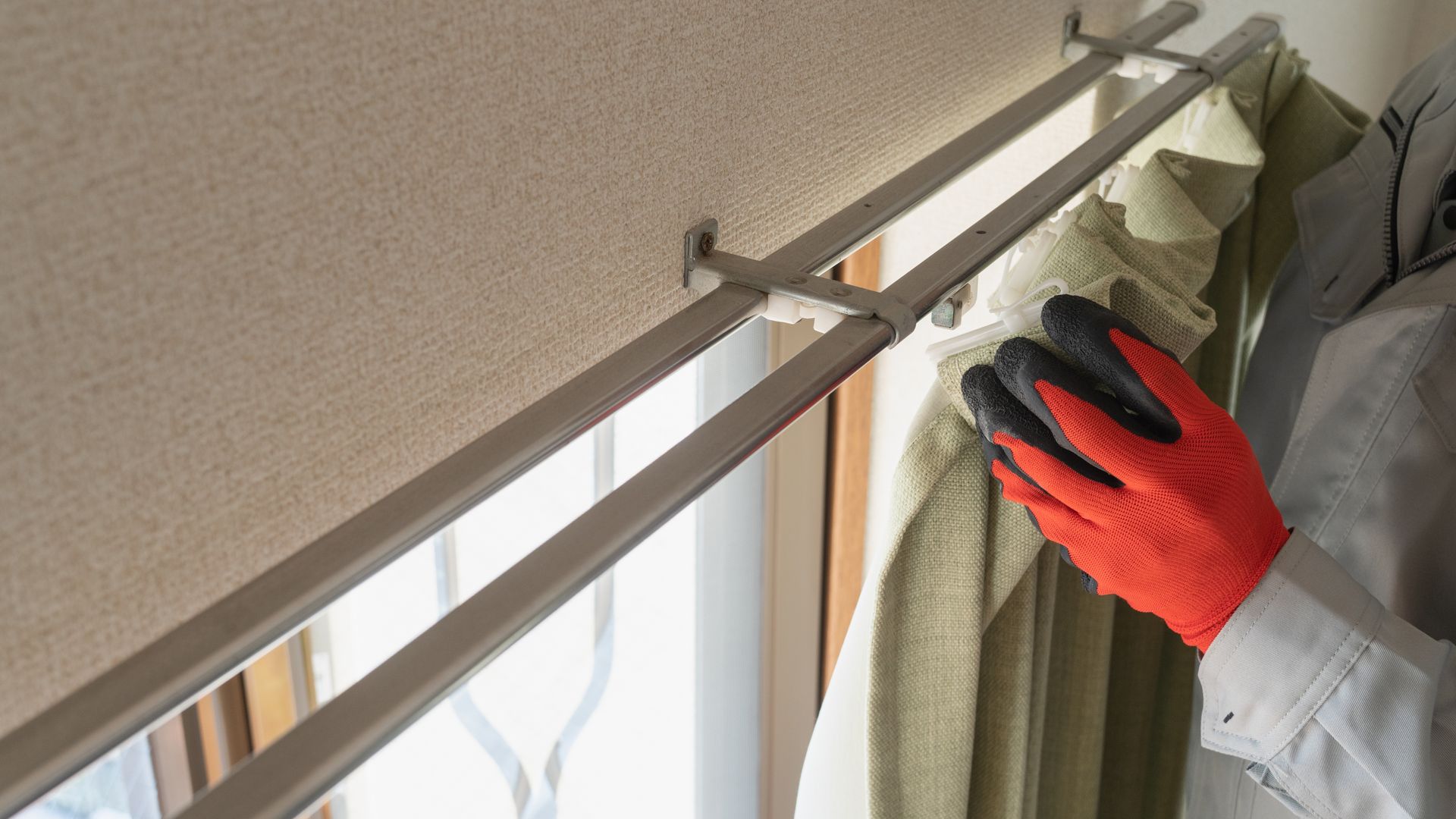 Person with orange gloves adjusting a light-green curtain on a silver rod