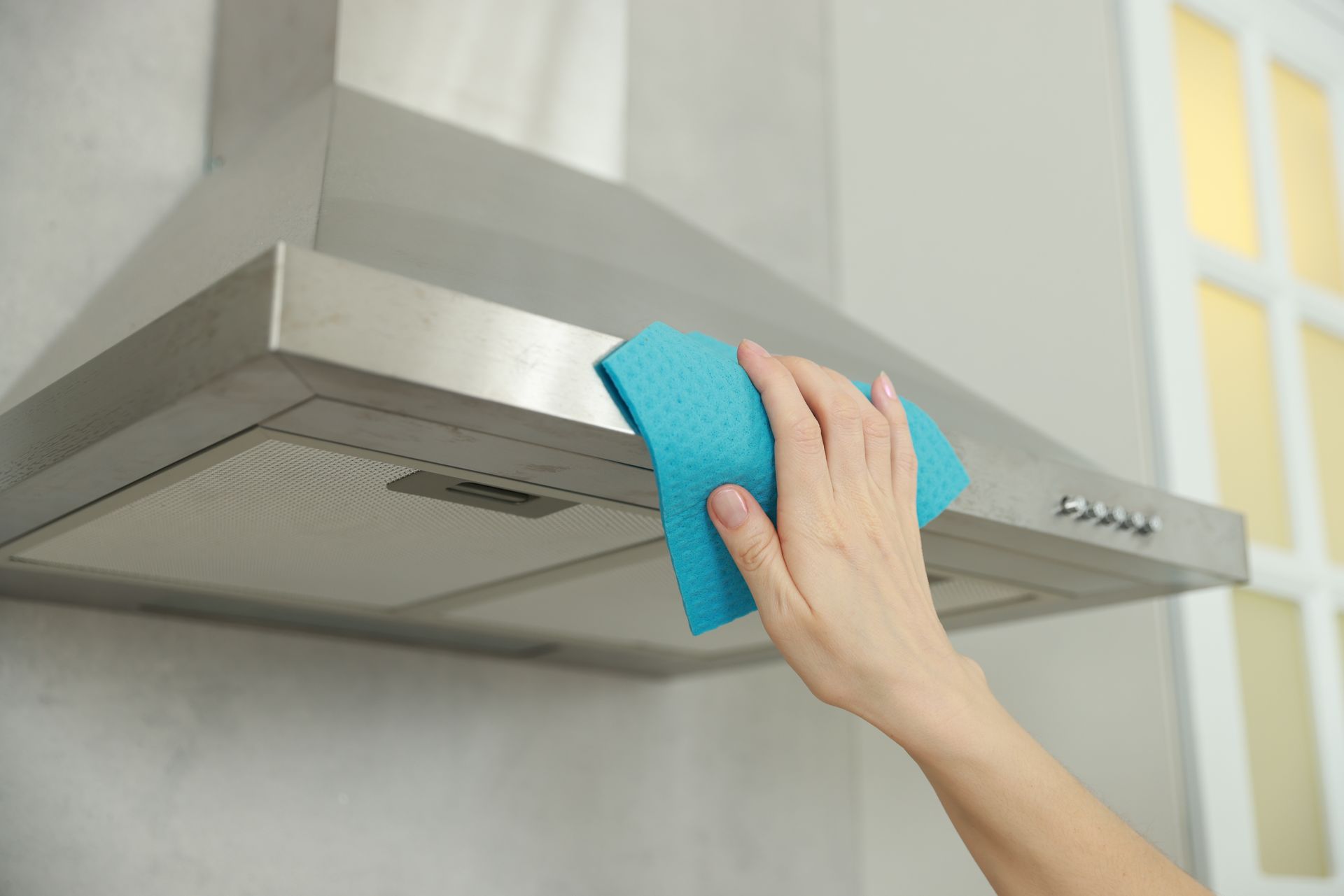 Person wiping a stainless steel range hood with a blue cloth in a kitchen