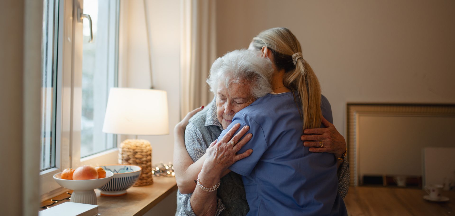 Woman in blue shirt embraces elderly person 