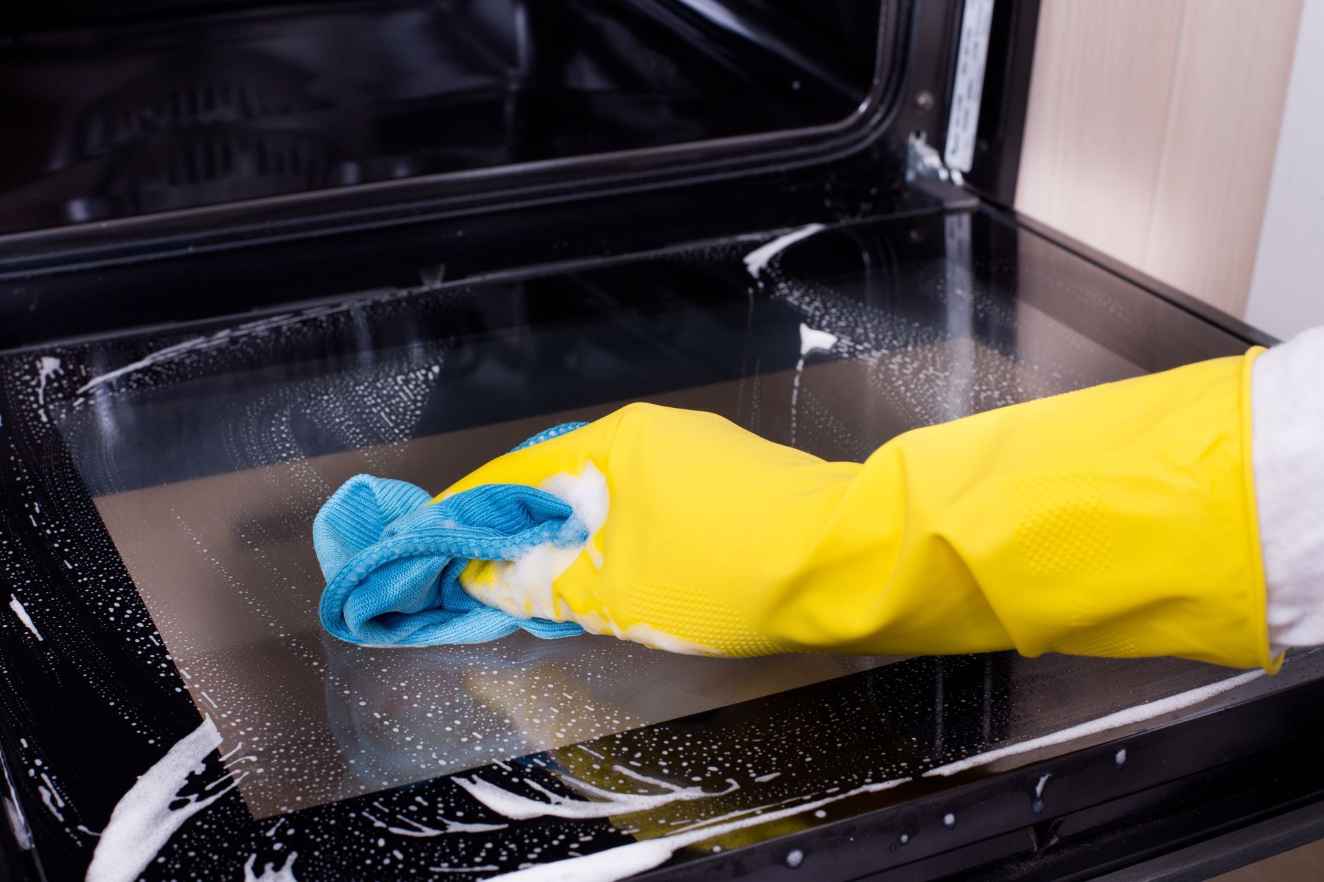 A person wearing a yellow glove cleans an oven door