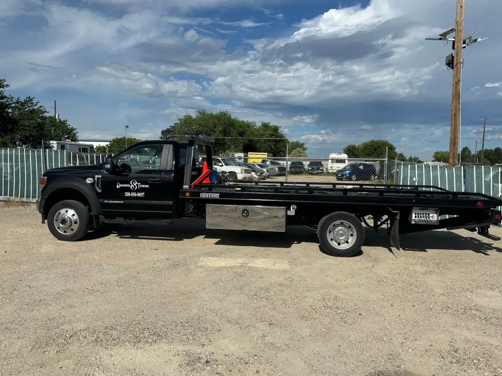 A black tow truck is parked in a gravel lot.