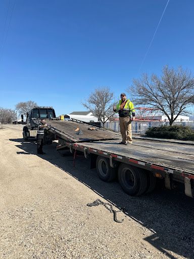 A man is standing on the back of a flatbed tow truck.