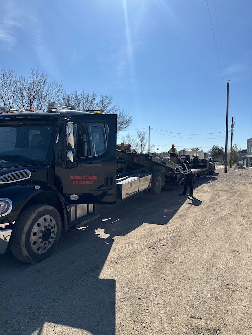 A tow truck is parked on the side of a dirt road.