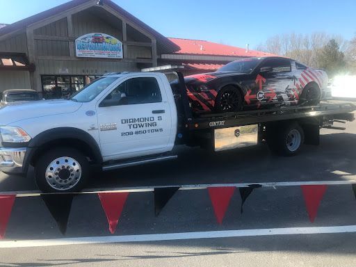 A tow truck is carrying a race car on the back of it.