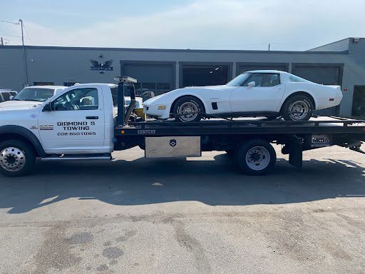 A white corvette is being towed by a tow truck.