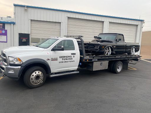 A tow truck is carrying a black car on the back of it.