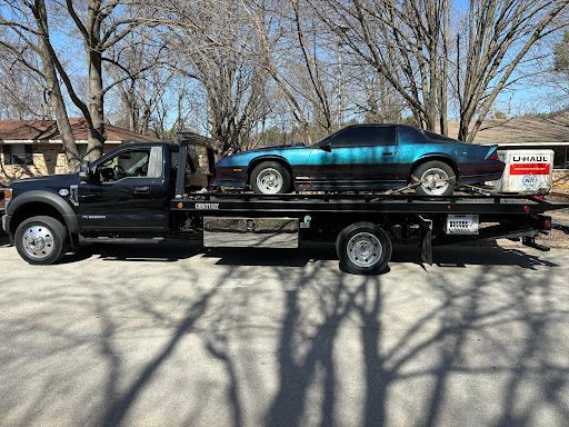 A tow truck is carrying two cars on the back of it.