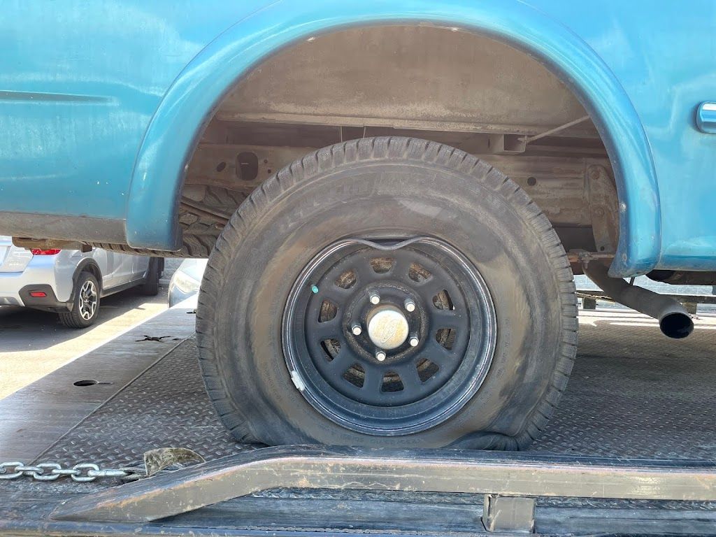 A blue truck with a flat tire is sitting on top of a tow truck.