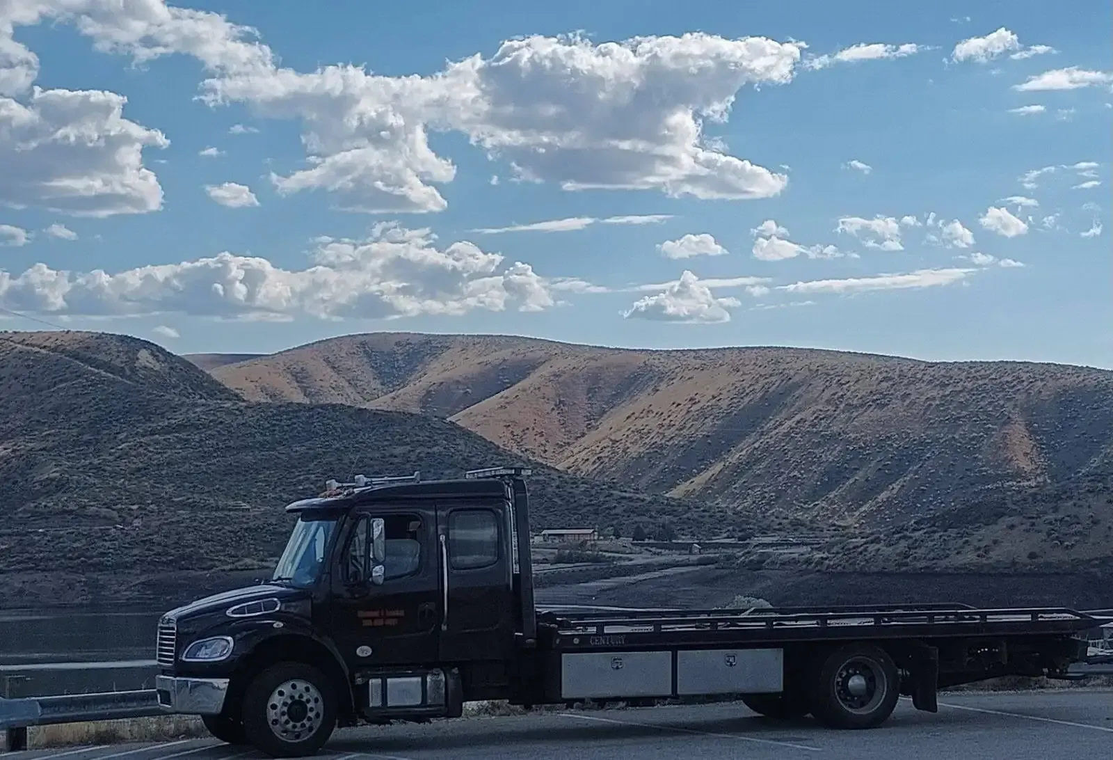 A tow truck is parked on the side of the road with mountains in the background.