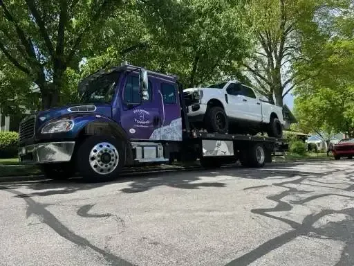 A tow truck is carrying a white truck on the back of it.