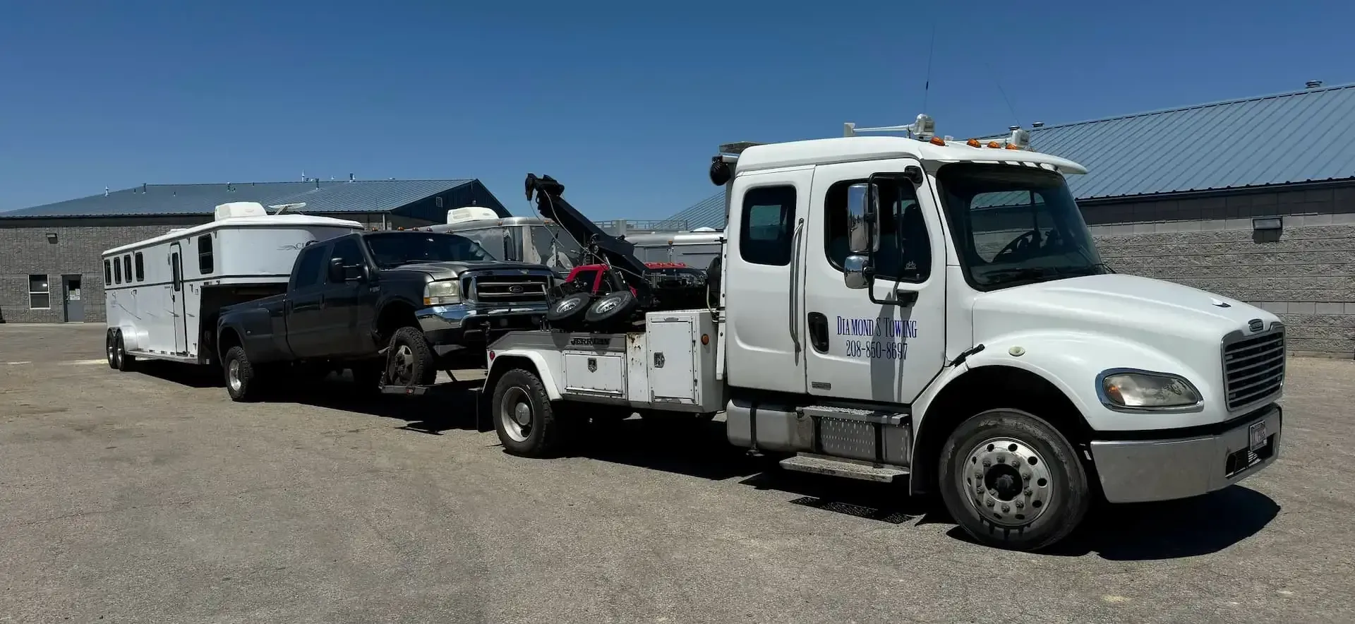 A white tow truck is towing a trailer and a truck.