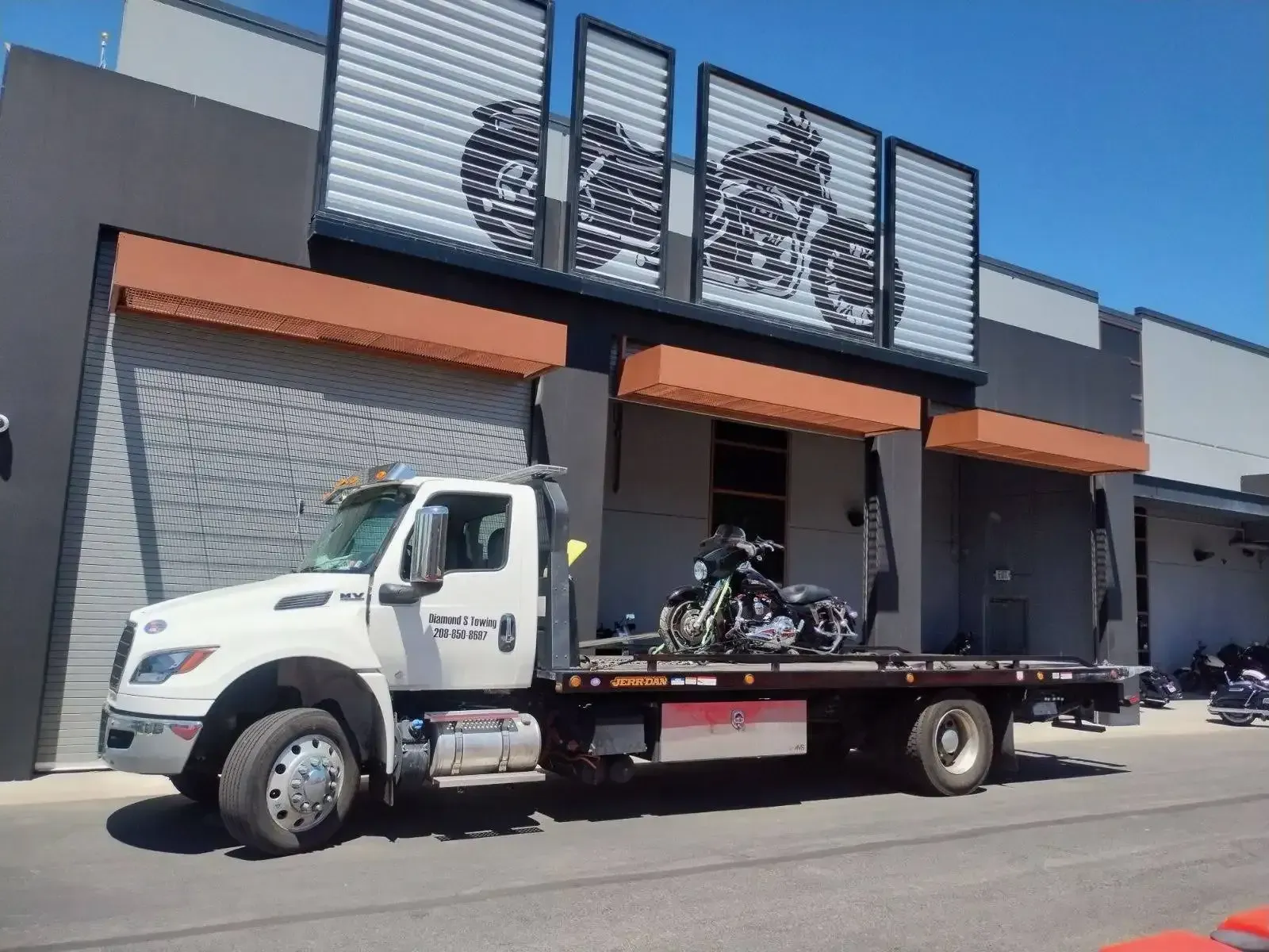A tow truck with a motorcycle on the back is parked in front of a building