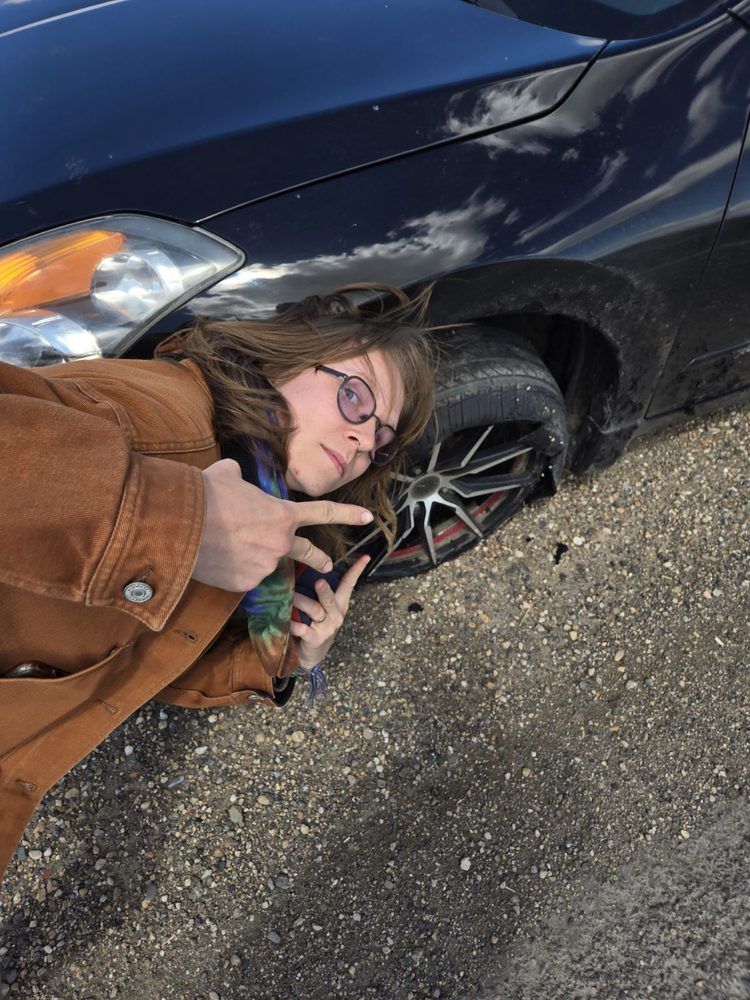 A woman is laying on the ground next to a car.