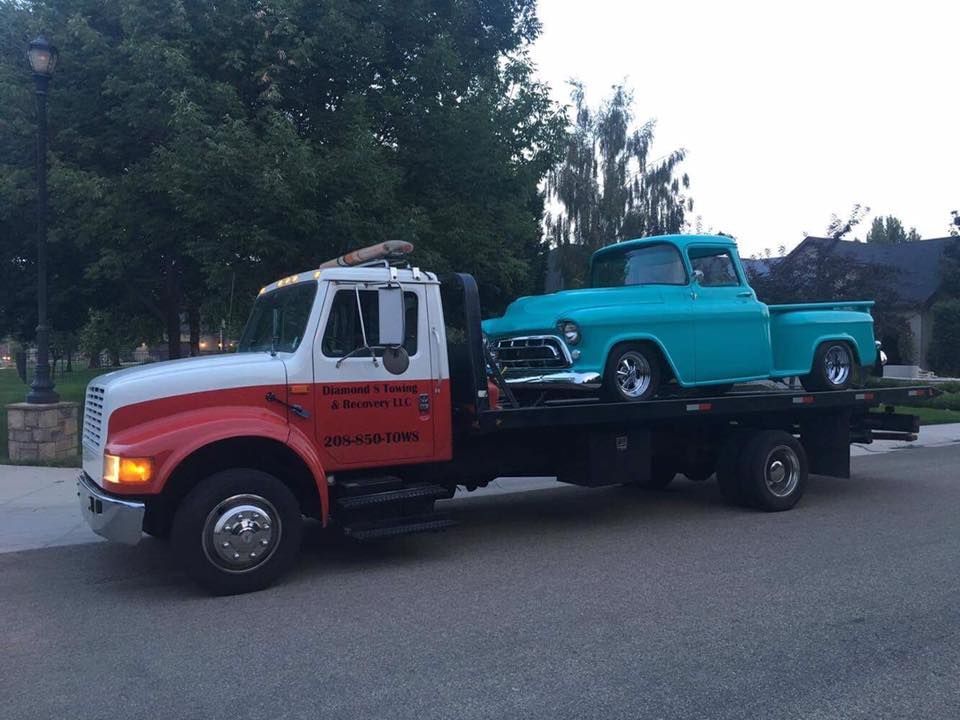 A red and white tow truck is carrying two pickup trucks