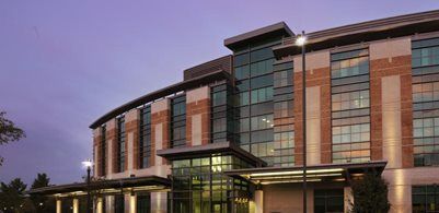 A multi-story building with a brick and glass facade, featuring a modern entrance canopy at twilight.