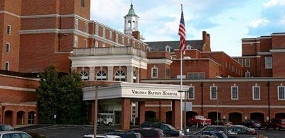 A brick building labeled Virginia Baptist Hospital, featuring a front entrance, a clock tower, and an American flag.
