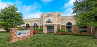 A tan brick Centra Urgent Care building with arched windows, surrounded by green lawns and trees under a blue sky.