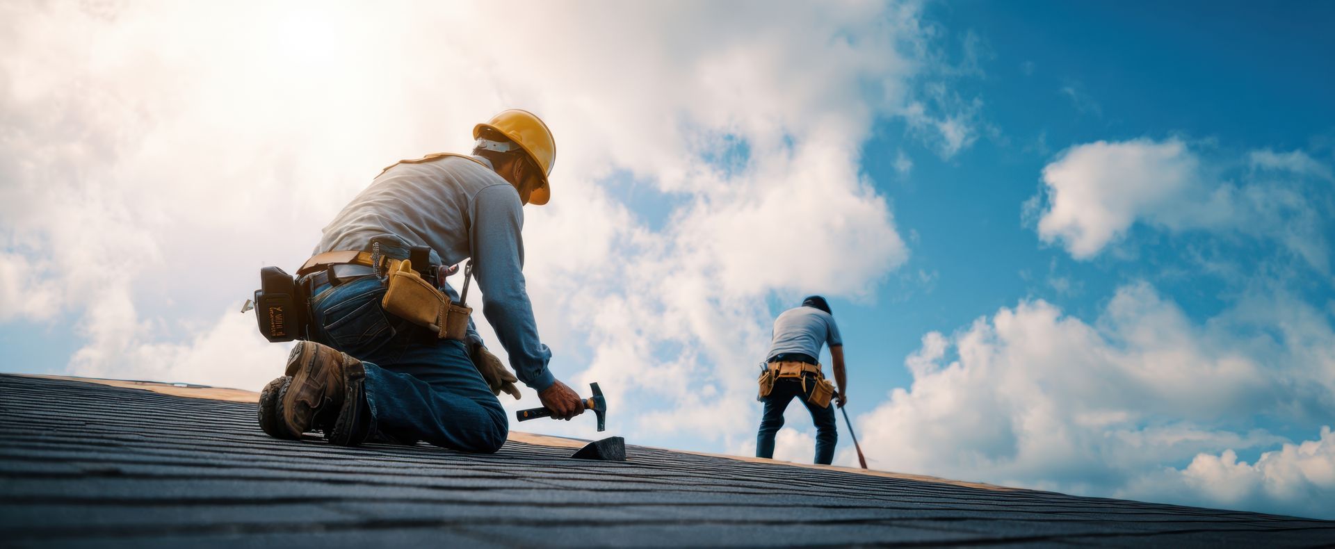 Workers installing roofing shingles under a bright sky.