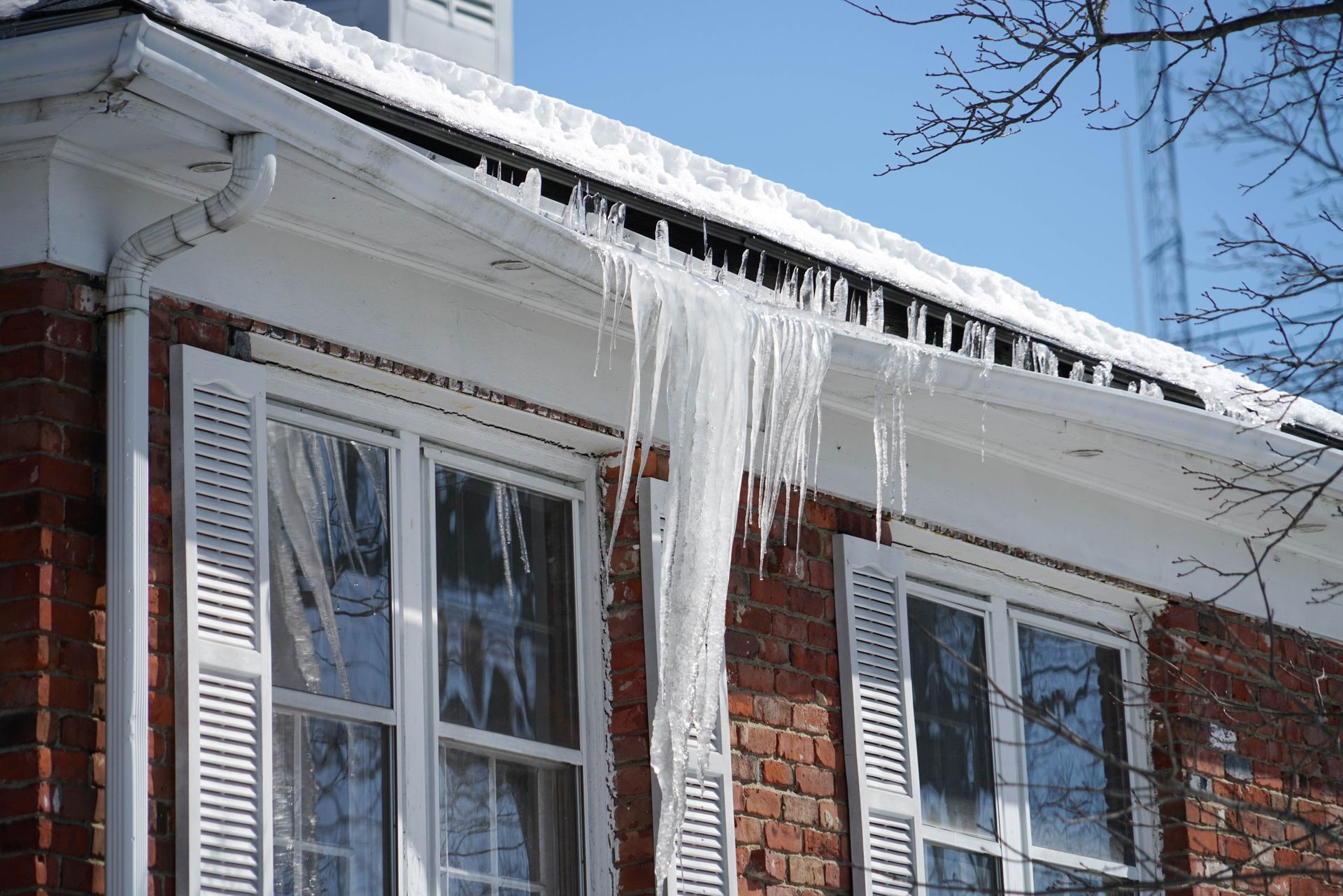 Large icicles hang from a snow-covered roof edge, showing ice dam damage above windows.