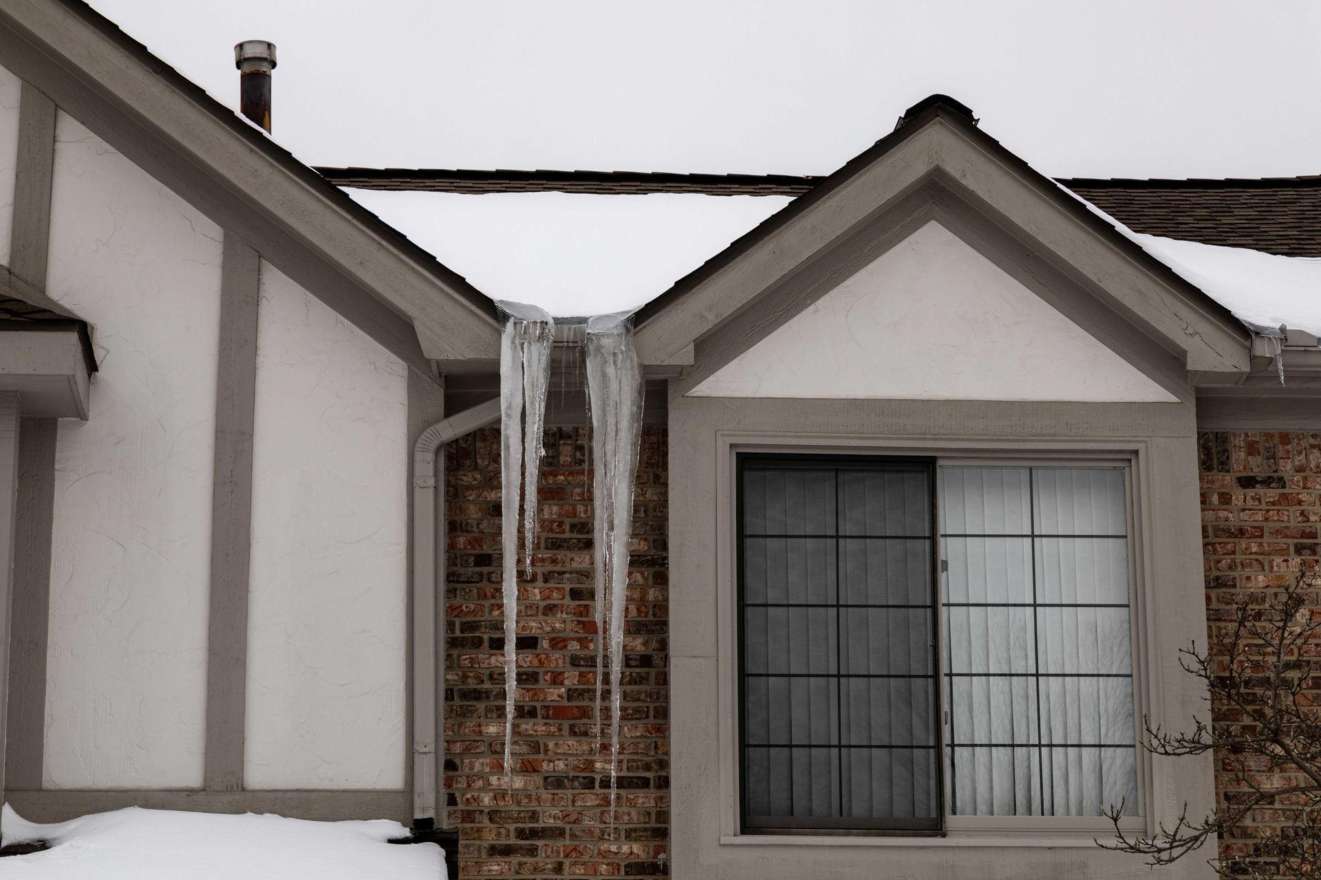 Long icicles spill from roof valleys, indicating ice dam buildup and potential roof damage.