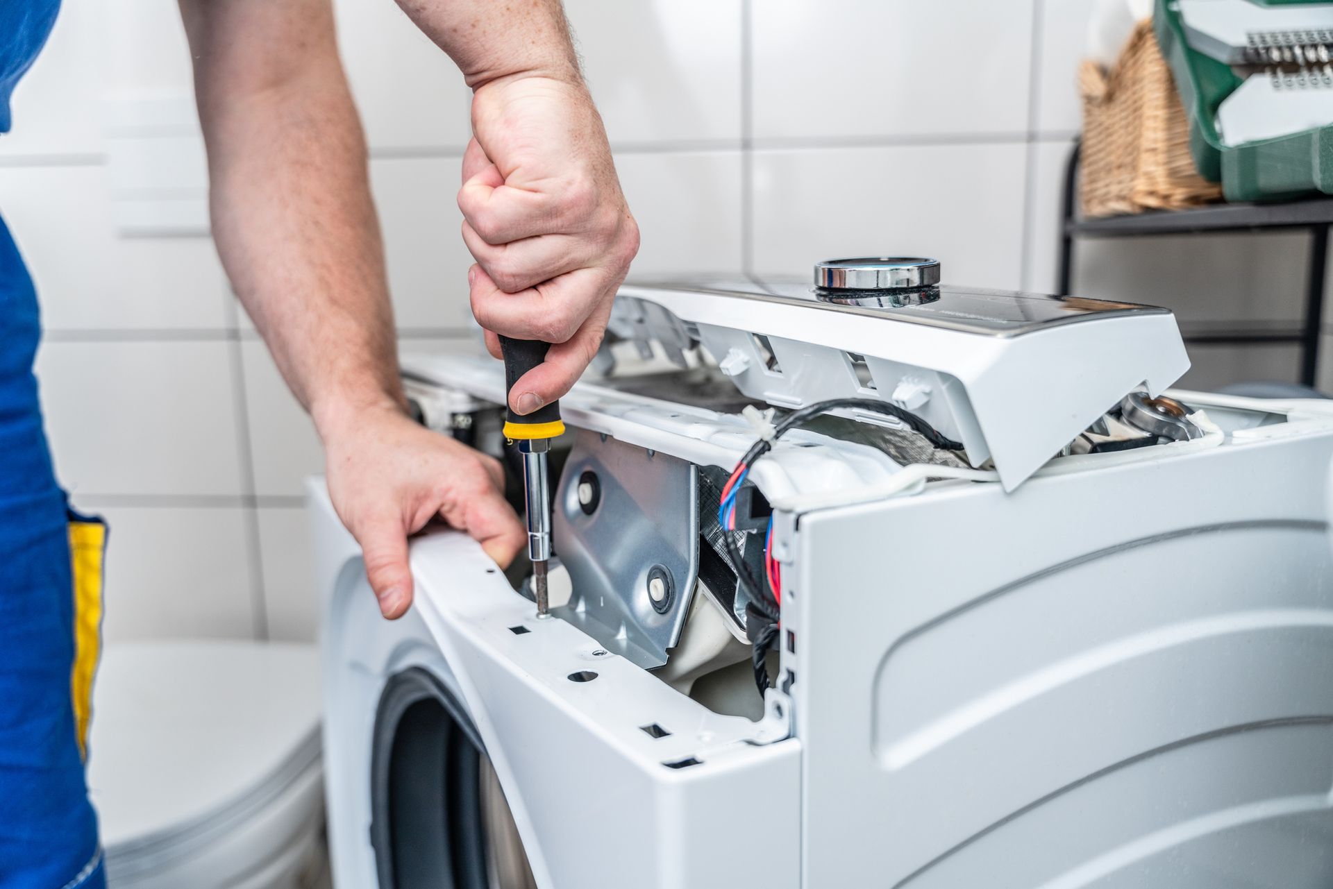 A man is fixing a washing machine with a screwdriver.