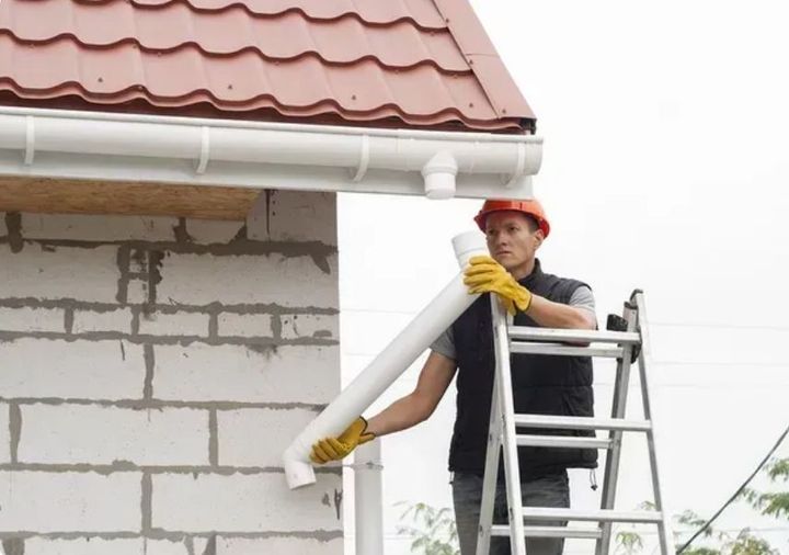 Worker inspecting a disconnected white downspout from a roof.