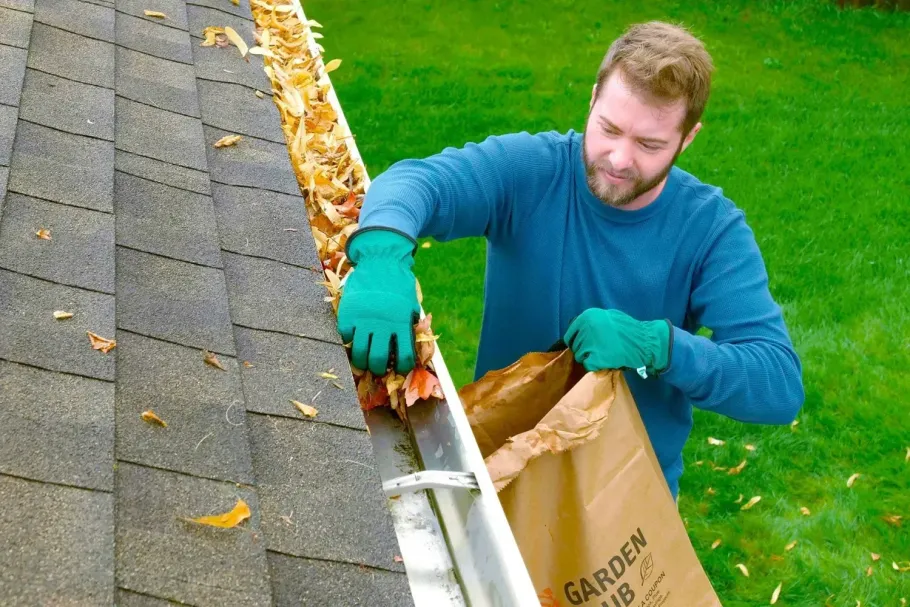 Man cleaning roof gutters and putting leaves into a bag.