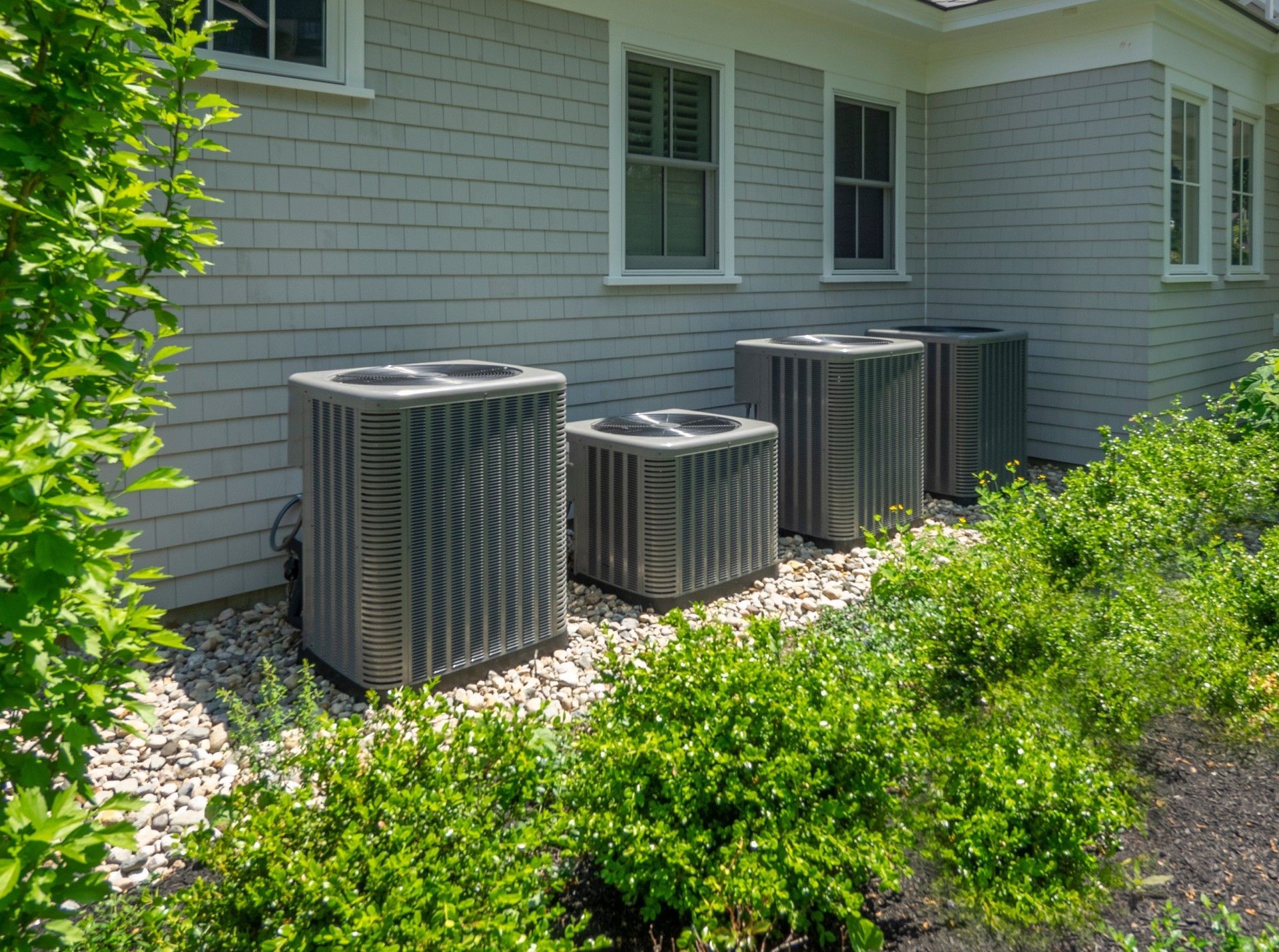 A row of air conditioners are sitting outside of a house.