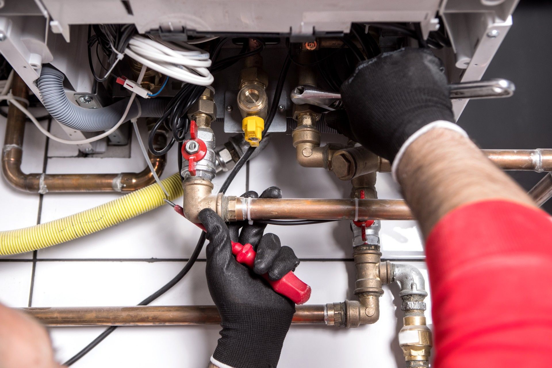 A plumber is working on a boiler with a wrench and a screwdriver.