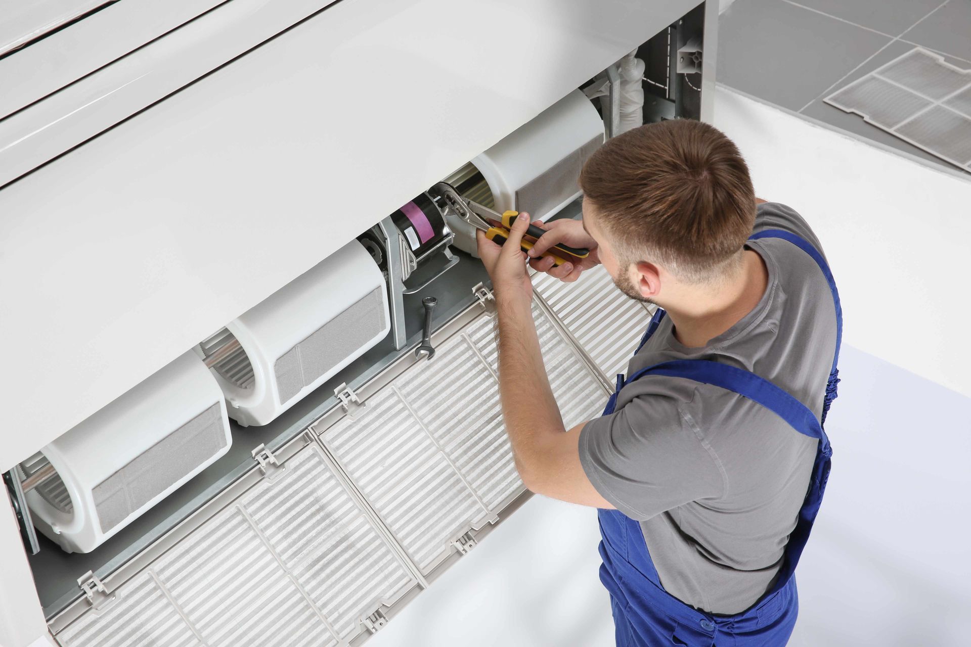 A man is working on an air conditioner with a screwdriver.