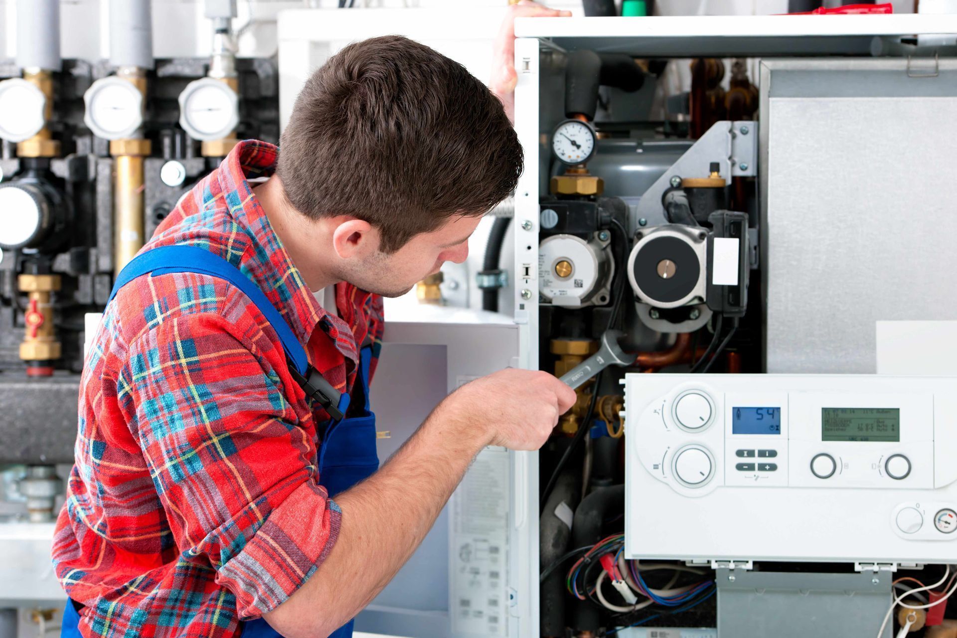 A man is working on a boiler with a wrench.