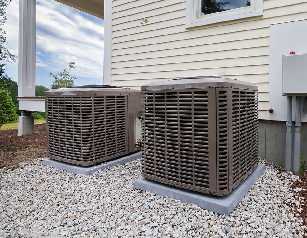 Two air conditioners are sitting outside of a house.