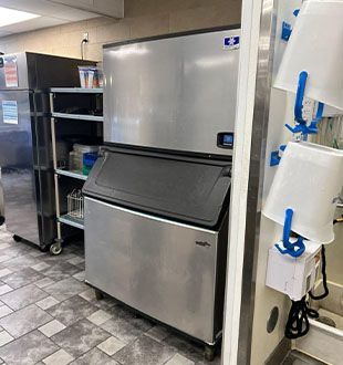 A stainless steel ice machine is sitting next to a refrigerator in a kitchen.
