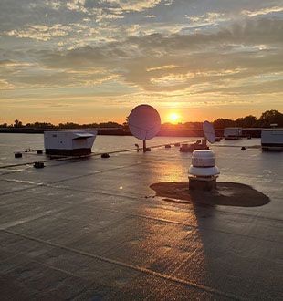 A rooftop with satellite dishes and a sunset in the background.