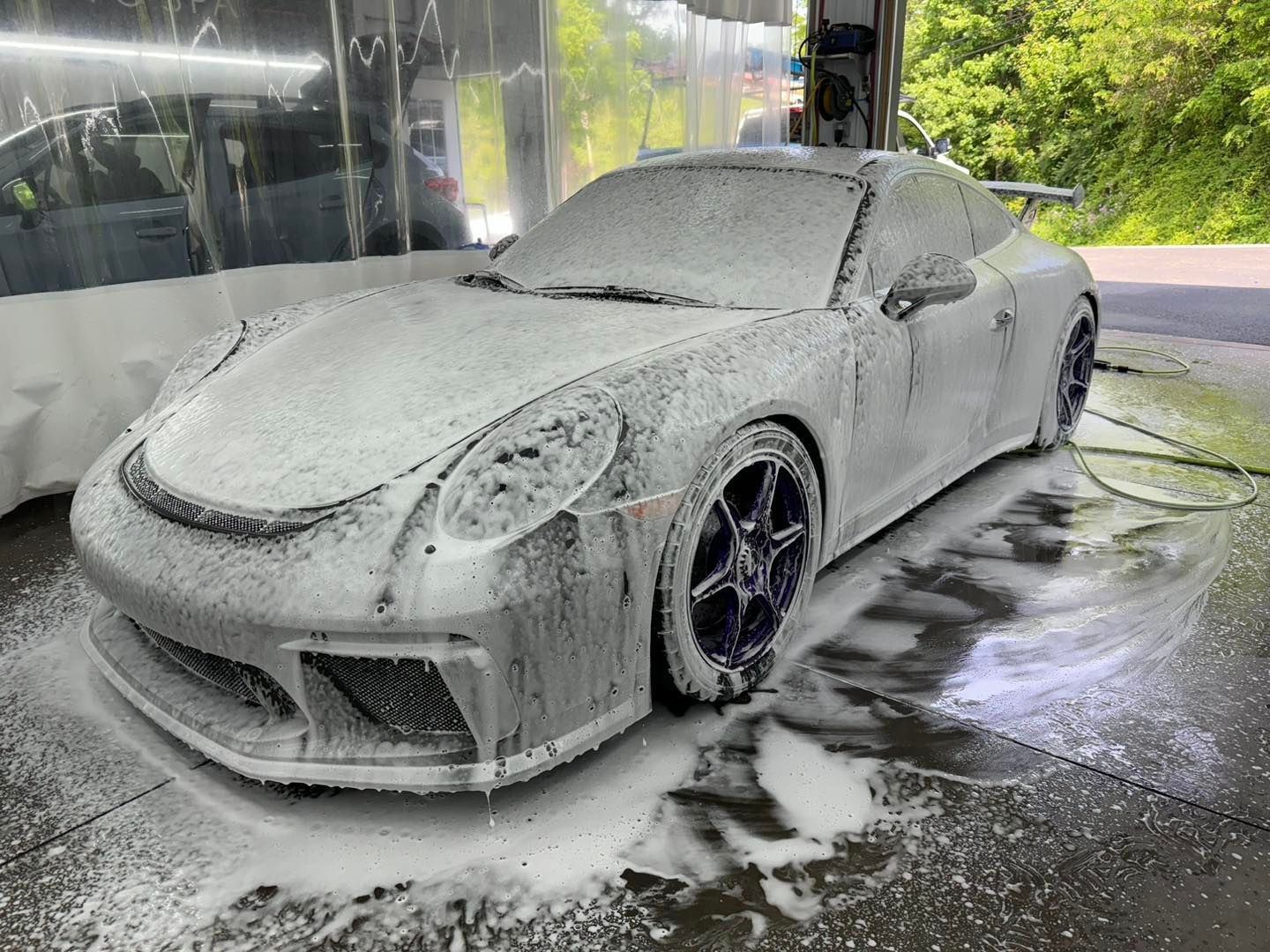 A porsche 911 is covered in foam at a car wash.