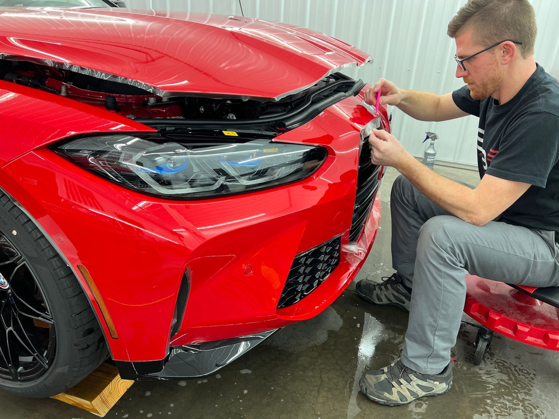 A man is applying a protective film to the front of a red car.