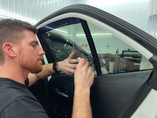 A man is applying a protective film to the front of a red car.
