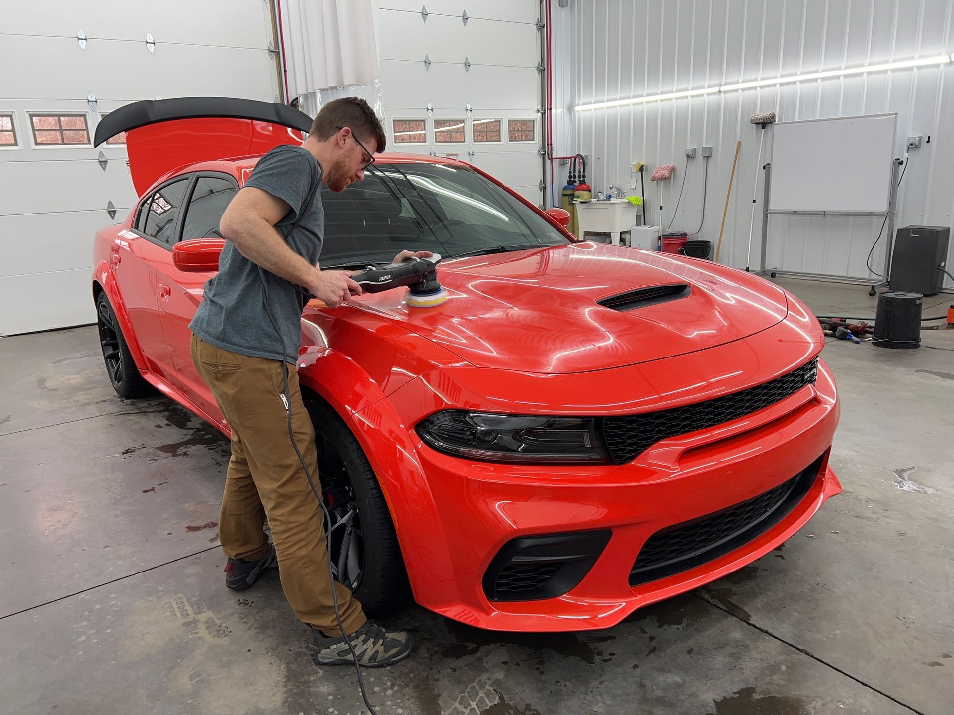 A man is polishing a red dodge charger in a garage.