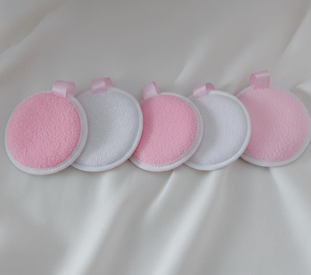 Tres discos desmaquillantes circulares y reutilizables, de color rosa y gris, con lazos adjuntos.