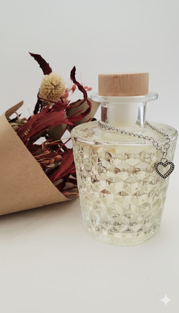 Tarro de cristal con copos de plata, corcho y colgante de corazón, junto a flores secas envueltas en papel marrón.