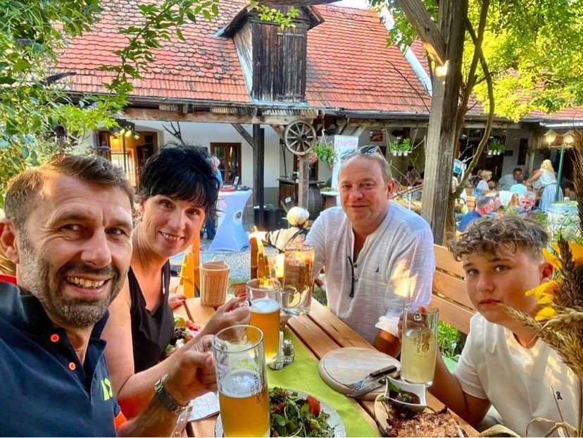 eine Gruppe von Personen sitzt bei sonnigem Wetter um einen Gasthaustisch