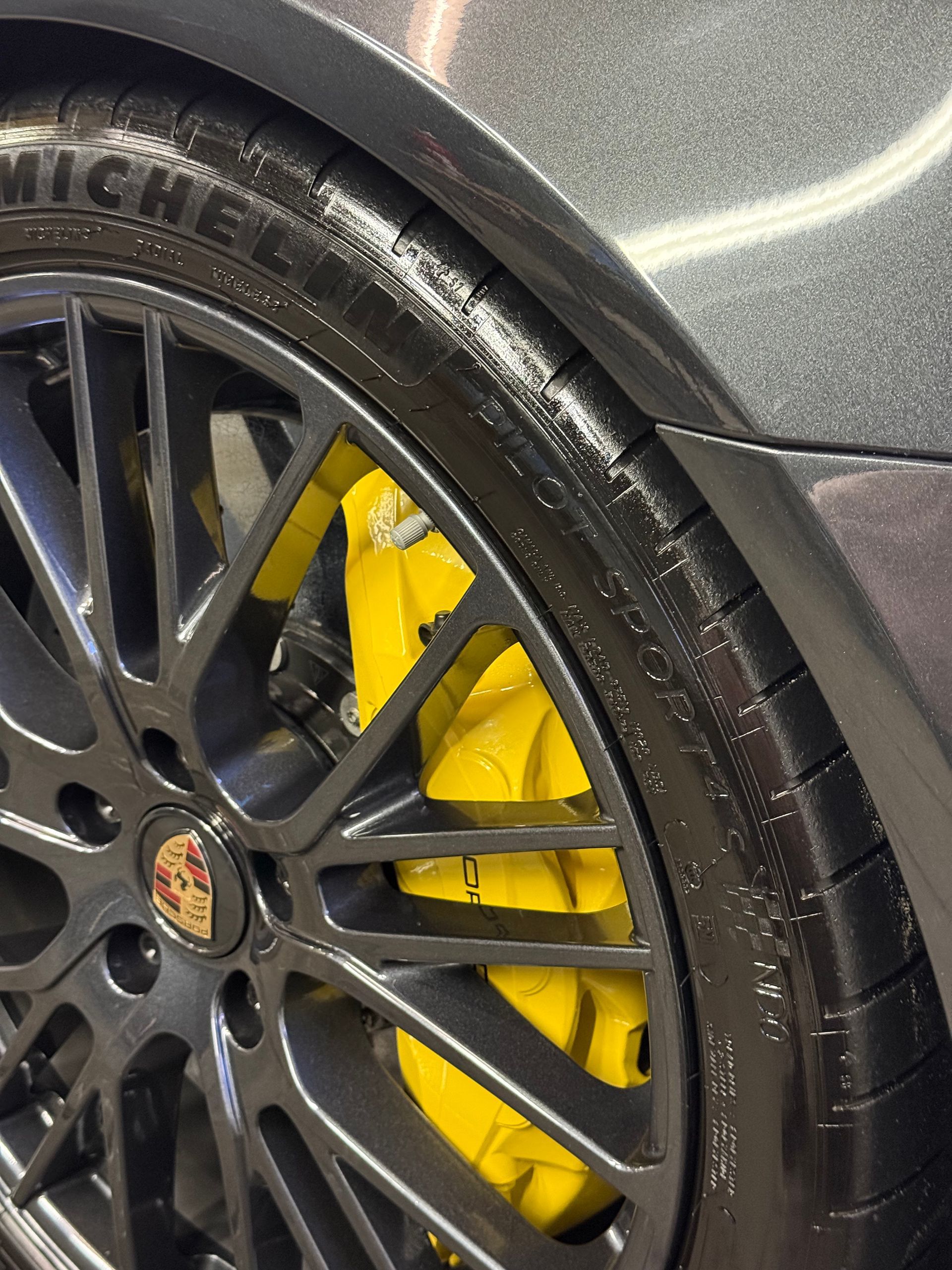 Donkergrijs autowiel met gele remklauwen en Porsche-logo.