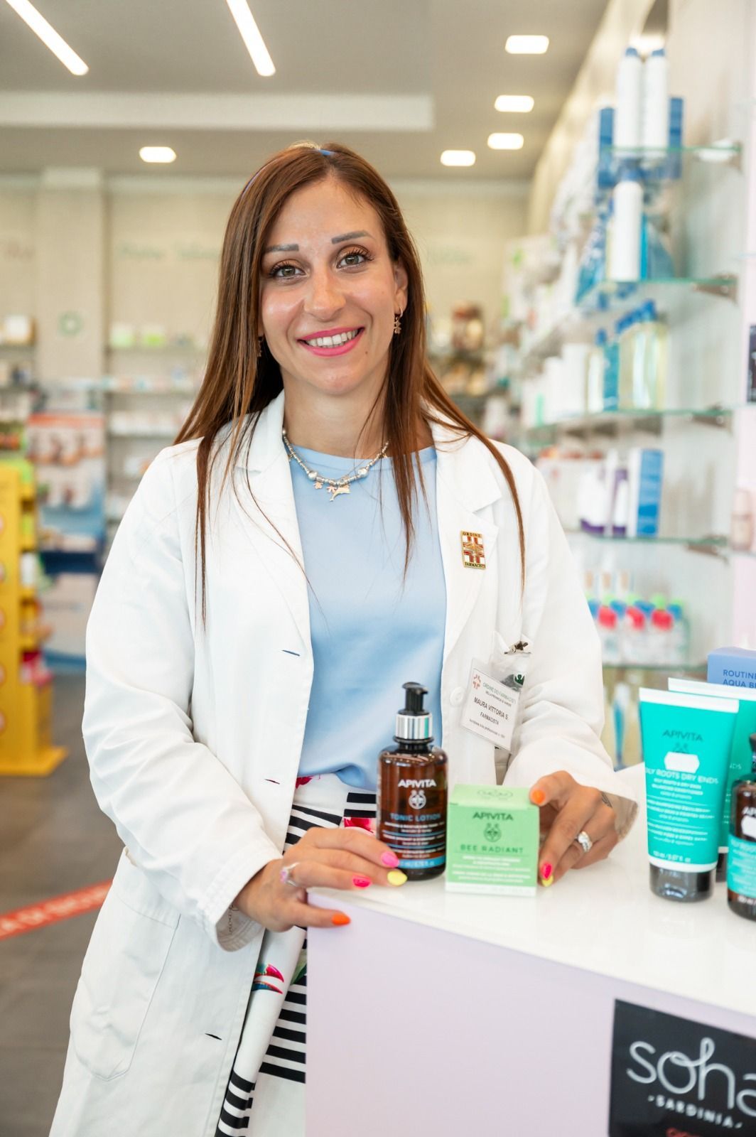 Una donna in camice è in piedi davanti al bancone di una farmacia.
