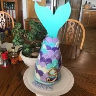 Mermaid tail birthday cake with teal fin and purple scales on a dining table